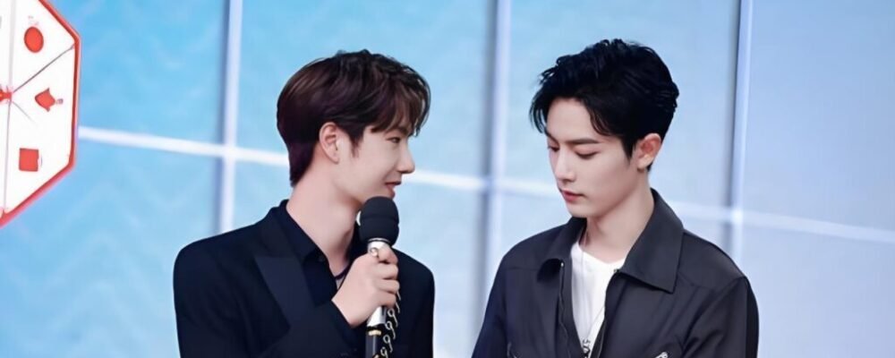 Fans holding signs in multiple languages at an overseas event, with Xiao Zhan and Wang Yibo on stage